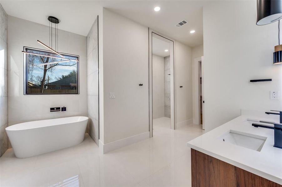 Spa-inspired bathroom featuring a freestanding soaking tub, large window with linear light fixture, dual vanity with undermount sinks, and separate shower enclosure
