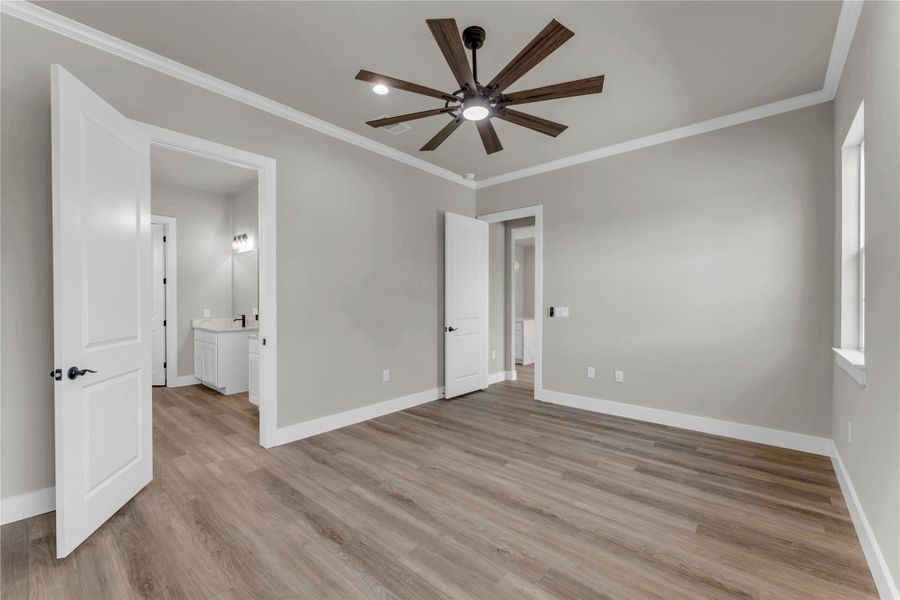 Unfurnished bedroom with ornamental molding, ceiling fan, light wood-type flooring, and ensuite bath