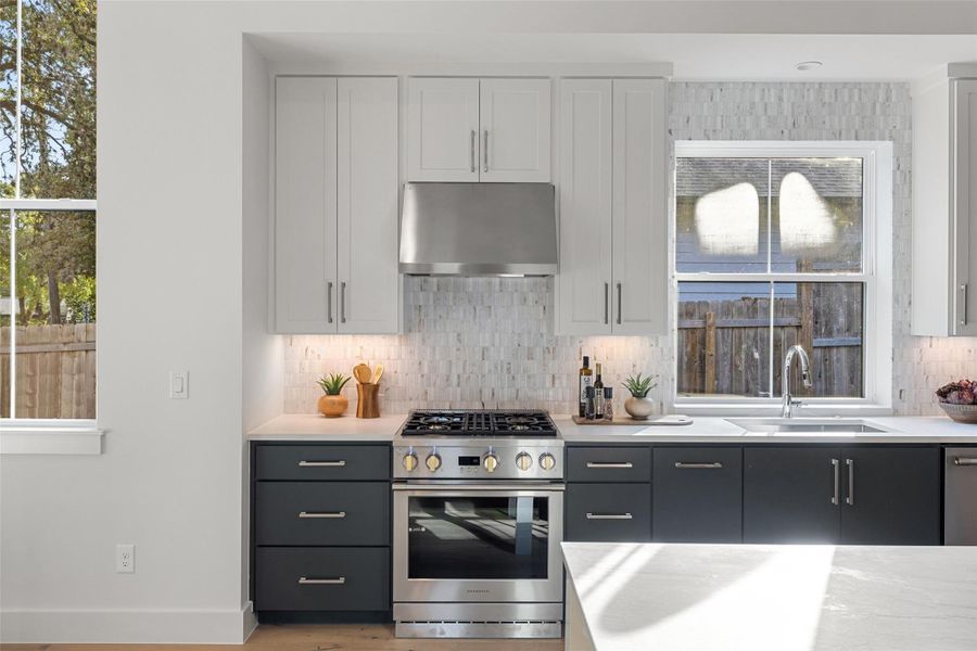 Kitchen featuring tasteful backsplash, range hood, white cabinetry, sink, and stainless steel appliances