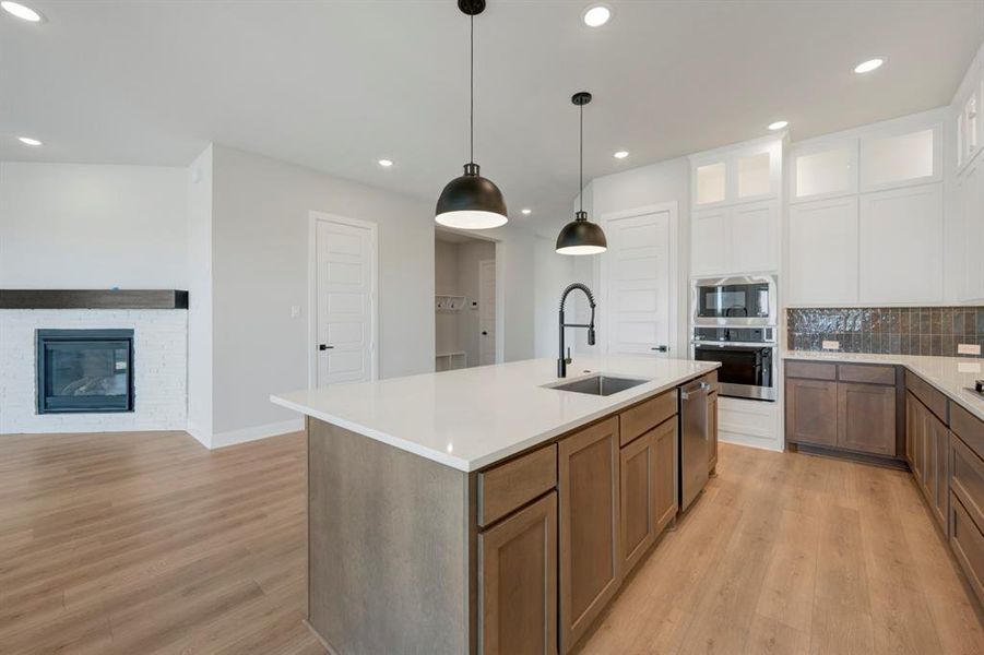 Two tone kitchen featuring tasteful backsplash, two tone cabinetry, pendant lighting, stainless steel appliances, and a fireplace