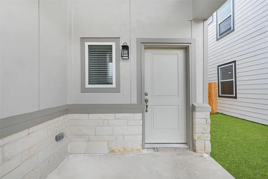 This photo shows a clean and modern entryway under a covered front porch area. It features a window and an outdoor light fixture and leads to a side yard with green grass.Please note: The image is not the actual home; it is a home with the same floor plan in the neighborhood. Finishes may vary. This photo shows a clean and modern entryway under a covered front porch area. It features a window and an outdoor light fixture and leads to a side yard with green grass.Please note: The image is not the actual home; it is a home with the same floor plan in the neighborhood. Finishes may vary.