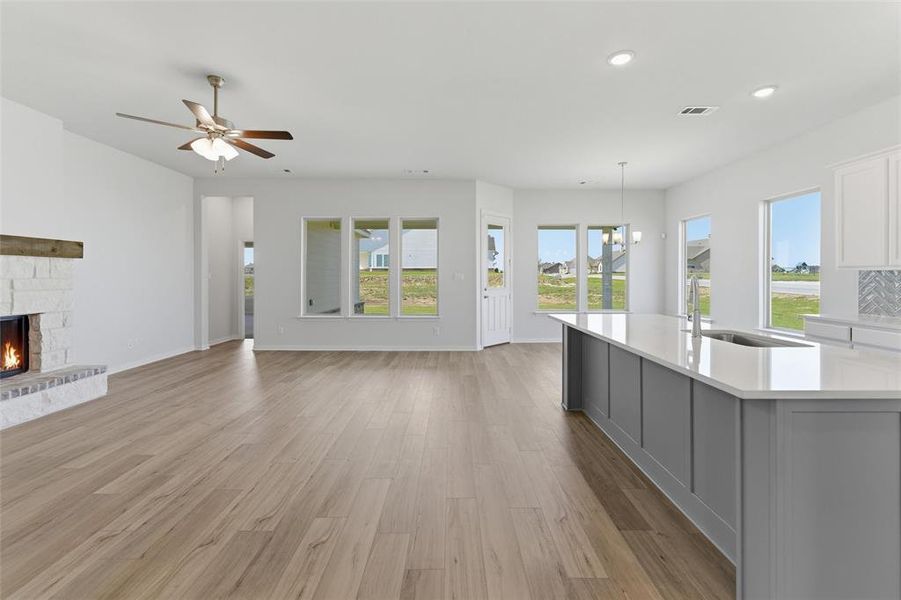 Open concept living space featuring wood-finish flooring, a white brick fireplace with a wood mantle, and an expansive kitchen island with a light-colored countertop