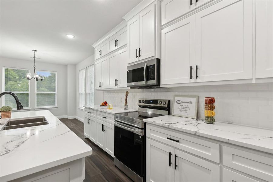 Kitchen with stainless steel appliances, a chandelier, white cabinetry, and sink