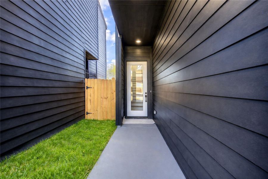 Gated exterior entrance with sleek dark siding. A glass door leads into the home. Perfect for a contemporary urban setting.