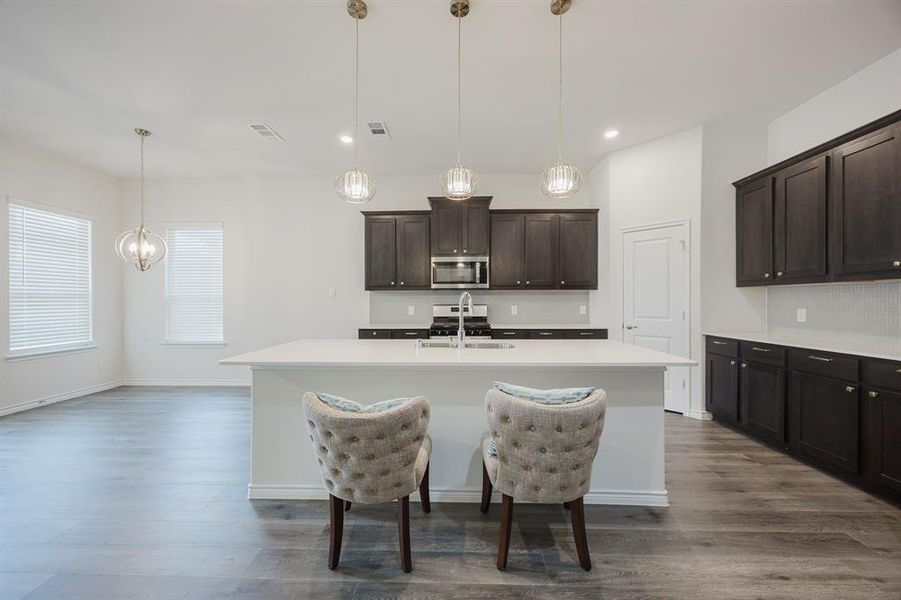 Kitchen with sink, hanging light fixtures, an island with sink, and decorative backsplash