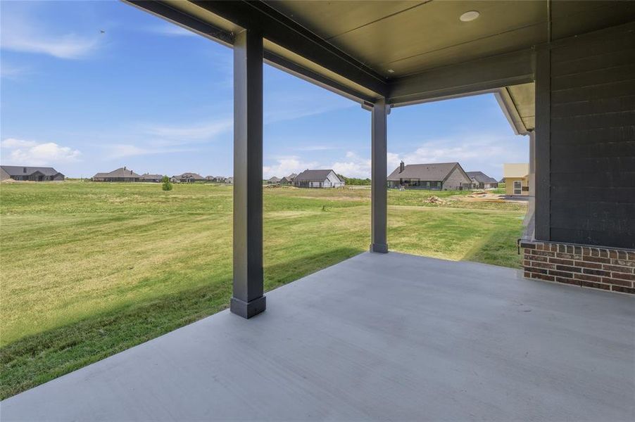 Covered outdoor patio with a concrete surface, supported by dark-toned columns Covered outdoor patio with a concrete surface, supported by dark-toned columns