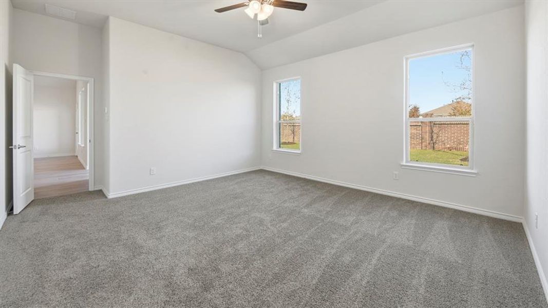 Spacious room featuring vaulted ceilings, a ceiling fan, two windows with backyard views, and plush gray carpeting