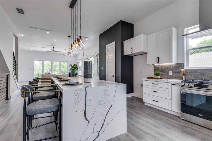 Kitchen featuring light hardwood / wood-style flooring, decorative light fixtures, stainless steel range, light stone countertops, and a center island