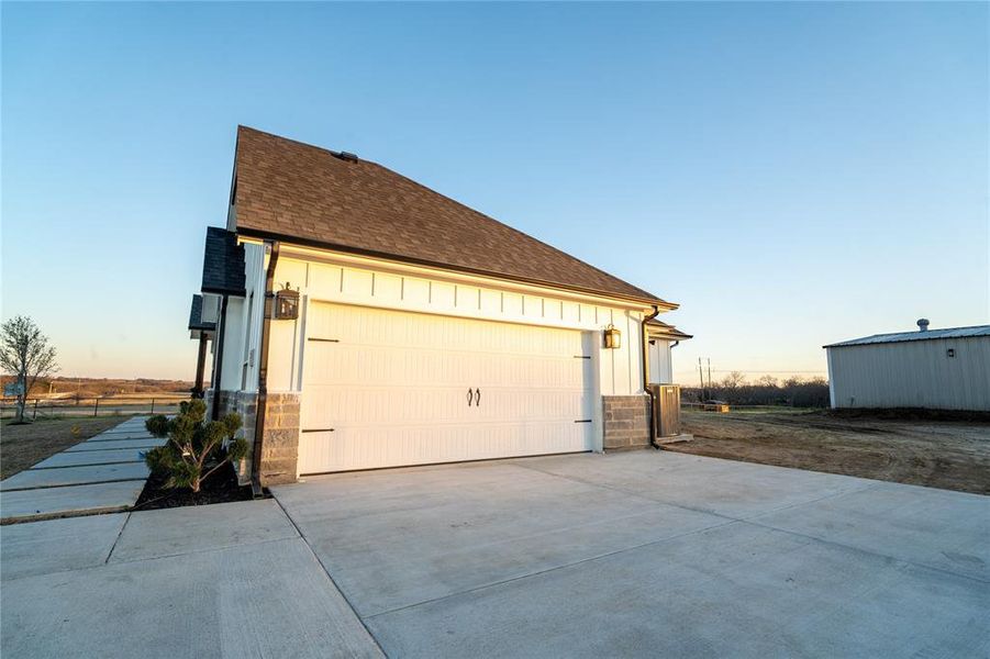 View of side of home with board and batten siding, stone siding, roof with shingles, and a garage