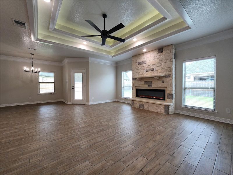 A striking stone fireplace anchors this spacious living area with elevated tray ceilings and wood-look tile flooring. A striking stone fireplace anchors this spacious living area with elevated tray ceilings and wood-look tile flooring.