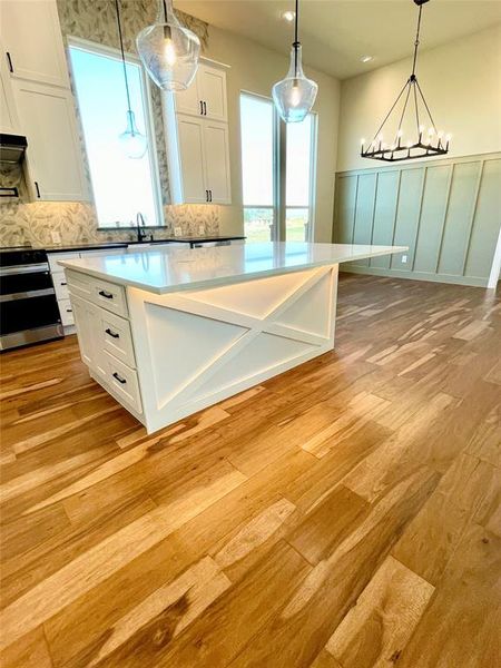 Kitchen featuring white cabinets, stainless steel stove, a spacious island, backsplash, and light wood-type flooring