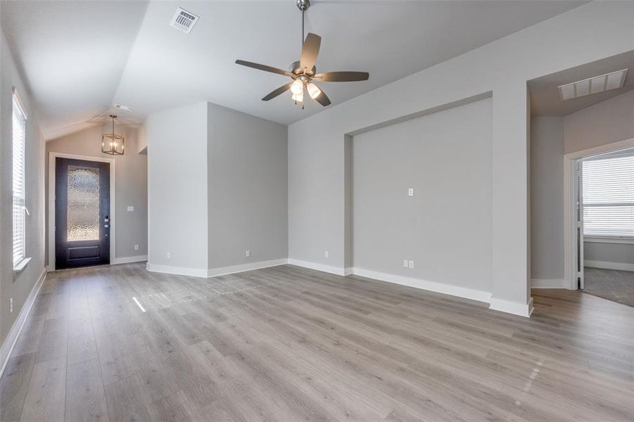 Unfurnished living room featuring a chandelier, light wood finished floors, a ceiling fan, and lofted ceiling