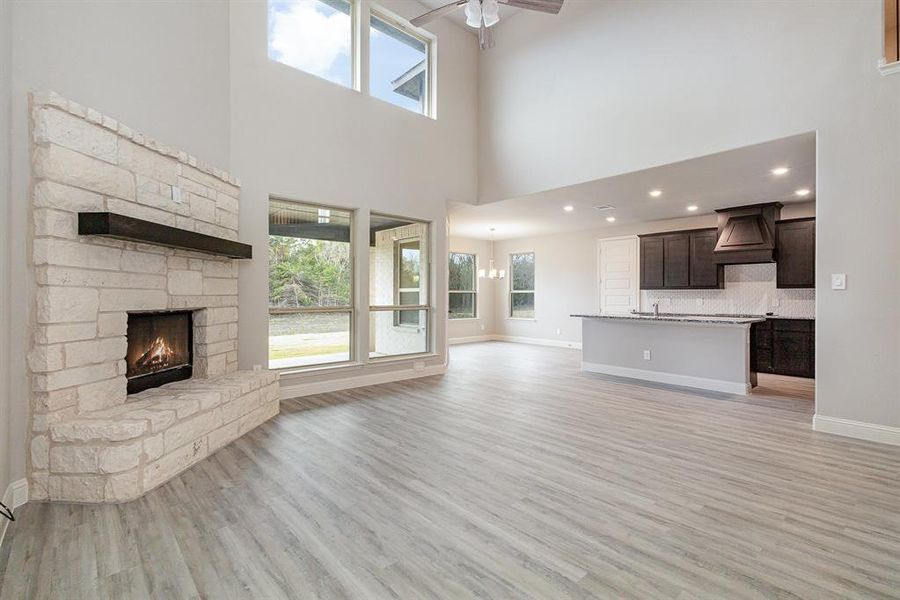 Unfurnished living room featuring light wood-type flooring, ceiling fan, sink, a high ceiling, and a stone fireplace