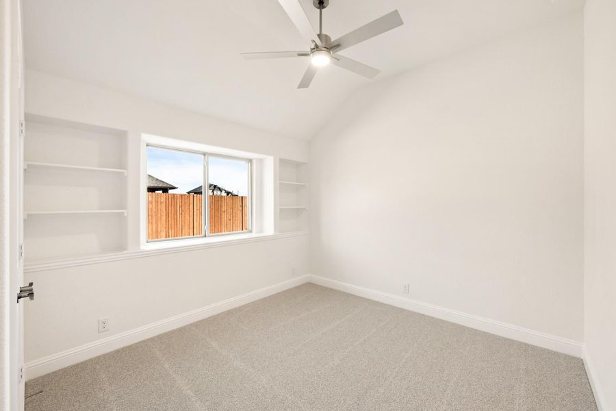 Empty bedroom with carpet, ceiling fan, built-in shelves, and a window overlooking a wood fence Empty bedroom with carpet, ceiling fan, built-in shelves, and a window overlooking a wood fence