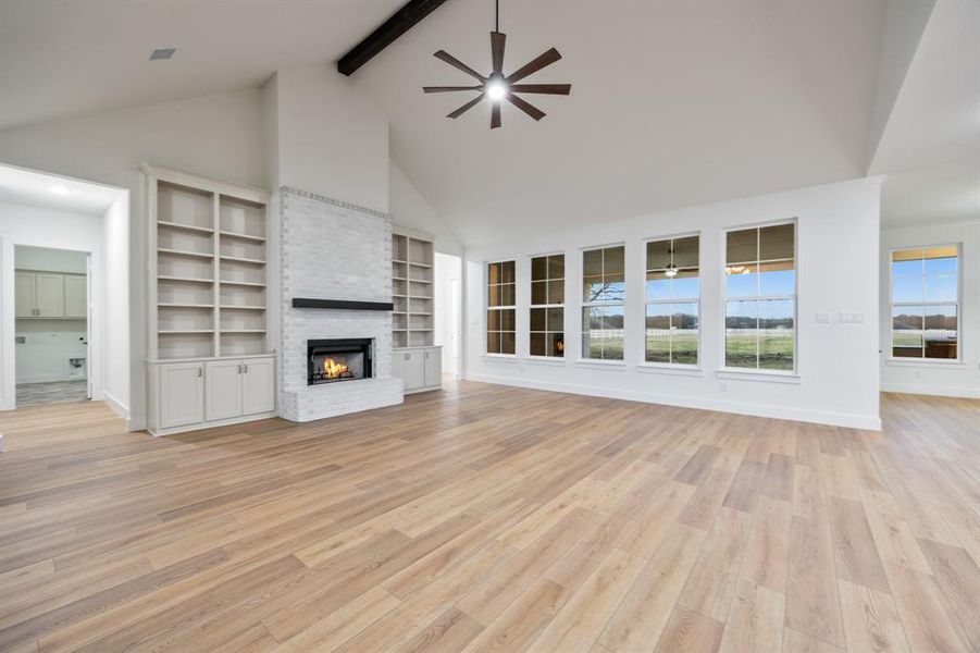 Unfurnished living room with high vaulted ceiling, a brick fireplace, light wood-style floors, ceiling fan, and built in features