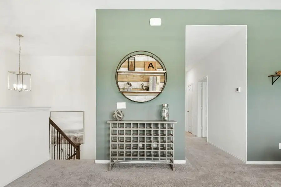 Upstairs hallway landing with green accent wall, round shelf mirror, decorative console table, and staircase railing nearby
