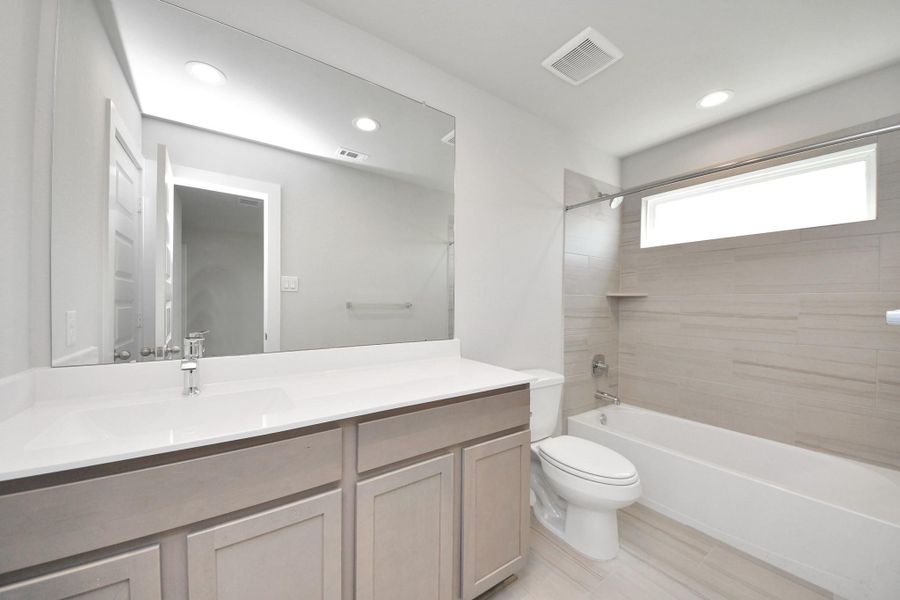 Secondary bath features tile flooring, bath/shower combo with tile surround, light stained wood cabinets, beautiful light countertop. Sample photo of completed home with similar floor plan. Actual colors and selections may vary.