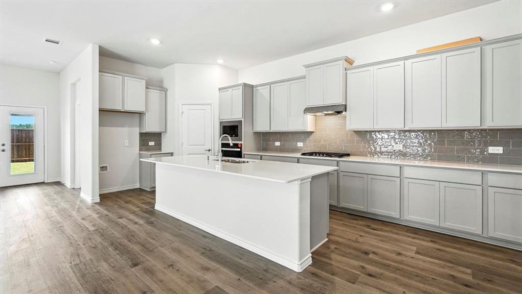 Kitchen with gray cabinetry, tasteful backsplash, a center island with sink, light stone counters, and recessed lighting
