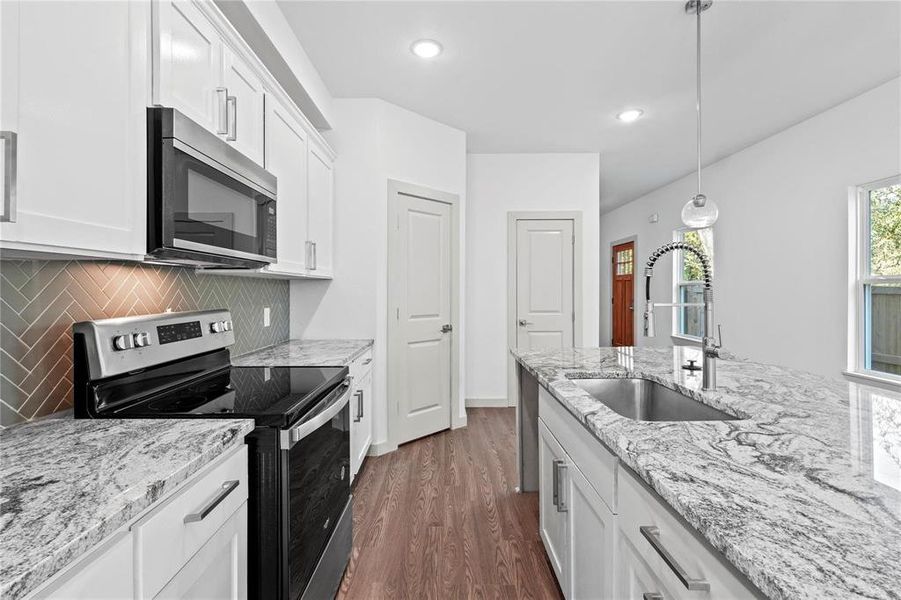 Kitchen with stainless steel appliances, white cabinets, decorative backsplash, light stone countertops, and recessed lighting