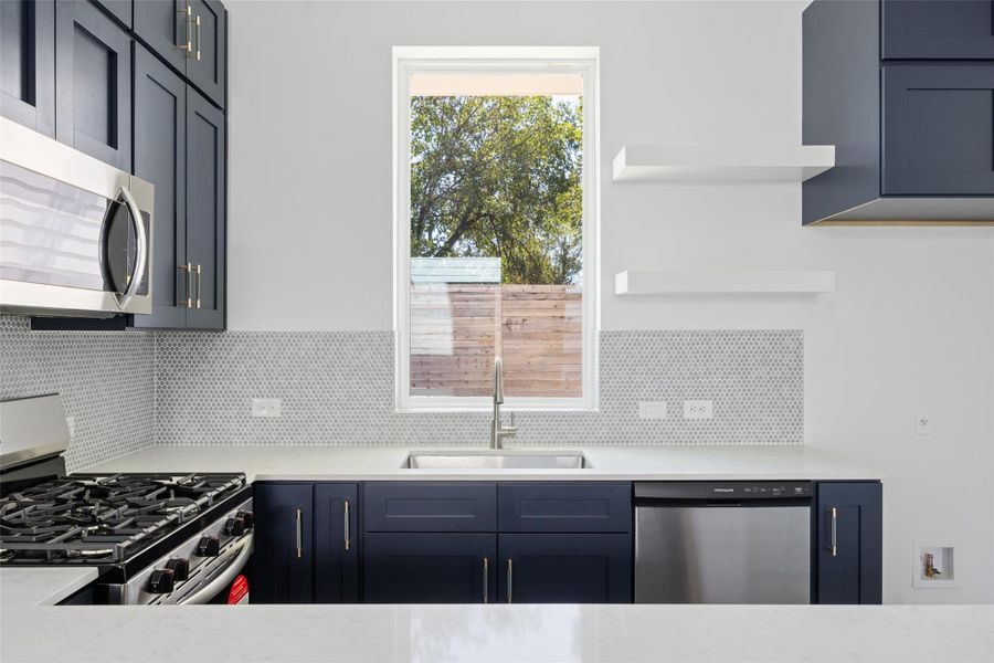 Kitchen featuring stainless steel appliances, open shelves, blue cabinets, and light stone counters Kitchen featuring stainless steel appliances, open shelves, blue cabinets, and light stone counters
