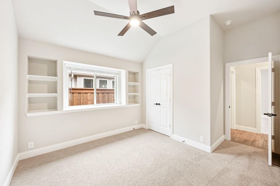 Empty bedroom with vaulted ceiling, ceiling fan, built-in shelves, carpet, and closet door Empty bedroom with vaulted ceiling, ceiling fan, built-in shelves, carpet, and closet door