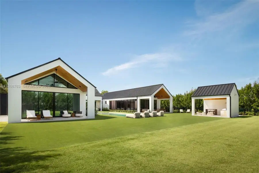 Modern exterior structures featuring white stucco siding, dark standing-seam metal roofing, vaulted wood-plank ceilings, expansive glass sliding doors, and a private swimming pool