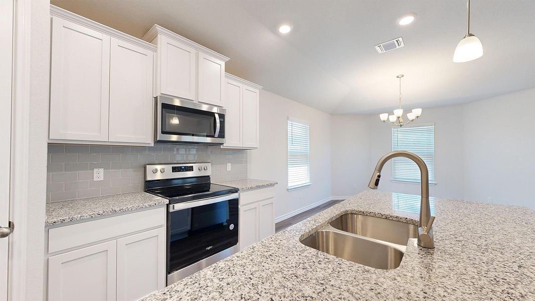Kitchen featuring stainless steel appliances, white cabinetry, backsplash, light stone countertops, and hanging lights Kitchen featuring stainless steel appliances, white cabinetry, backsplash, light stone countertops, and hanging lights