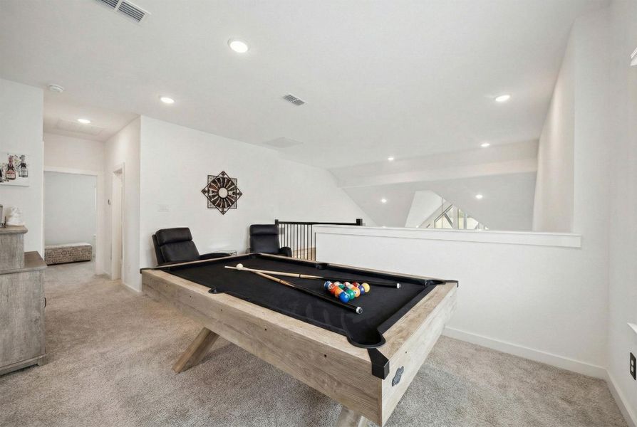 THE UPSTAIRS SPACE IS CONFIGURED AS A GAME ROOM WITH CARPETED FLOORS AND A VIEW OF THE LOWER LIVING SPACE.