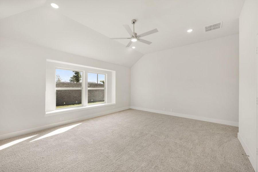Empty bedroom with vaulted ceiling, ceiling fan, carpet flooring, and large window Empty bedroom with vaulted ceiling, ceiling fan, carpet flooring, and large window
