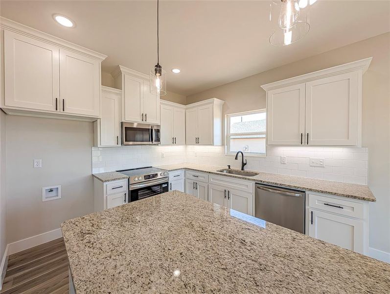 Kitchen with appliances with stainless steel finishes, dark wood-style floors, white cabinets, light stone counters, and recessed lighting Kitchen with appliances with stainless steel finishes, dark wood-style floors, white cabinets, light stone counters, and recessed lighting