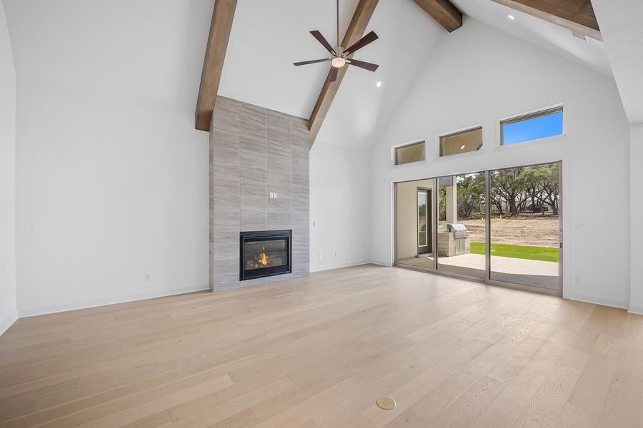 Unfurnished living room with high vaulted ceiling, ceiling fan, a fireplace, light wood-style flooring, and beam ceiling