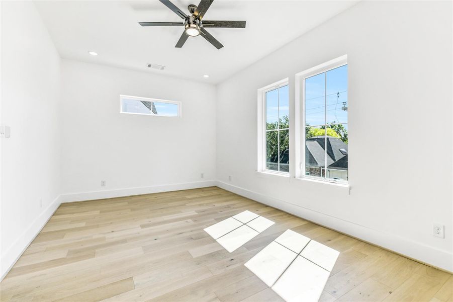 This view showcases the architectural symmetry and light-filled design of the space. The clerestory window adds privacy while maintaining brightness, and the crisp white walls serve as the perfect canvas for personal style. A modern ceiling fan with integrated lighting and recessed LED fixtures ensure comfort and functionality year-round.