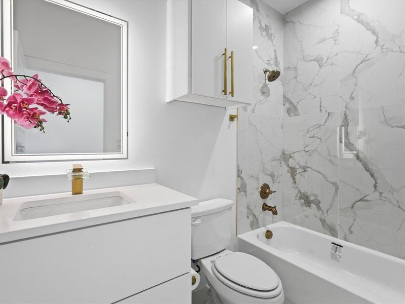 Bathroom featuring a white vanity with integrated sink, gold-finish faucet, and an illuminated mirror