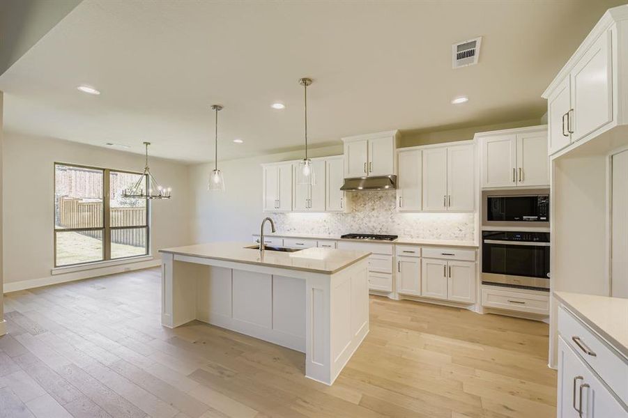 Kitchen with backsplash, stainless steel appliances, a center island with sink, decorative light fixtures, and white cabinetry