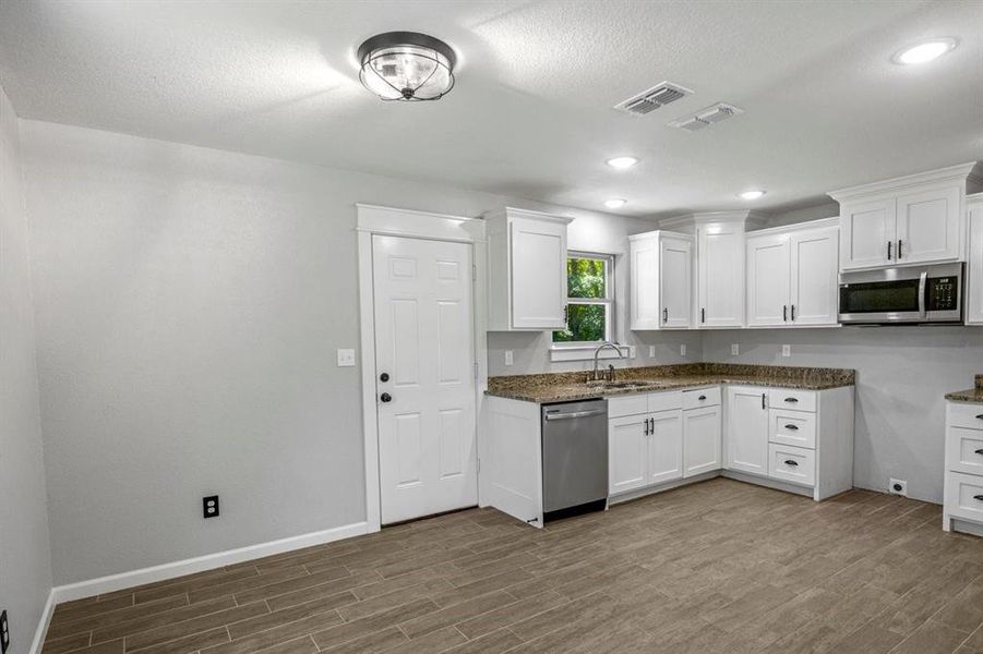 Kitchen featuring white cabinets, stainless steel appliances, wood tiled floors, recessed lighting, and dark stone countertops Kitchen featuring white cabinets, stainless steel appliances, wood tiled floors, recessed lighting, and dark stone countertops