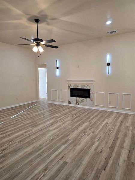 Unfurnished living room featuring light wood-type flooring, a fireplace, and a ceiling fan Unfurnished living room featuring light wood-type flooring, a fireplace, and a ceiling fan