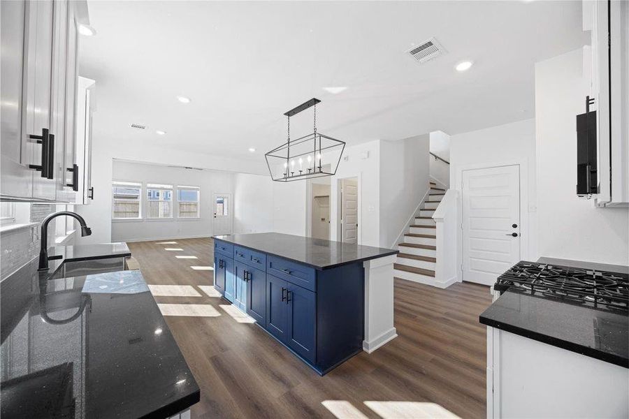 Bright, modern kitchen with quartz countertops and a striking blue island. The space features white cabinetry, stainless steel appliances, and wood look flooring, leading to an open living area with large windows and a staircase. Bright, modern kitchen with quartz countertops and a striking blue island. The space features white cabinetry, stainless steel appliances, and wood look flooring, leading to an open living area with large windows and a staircase.