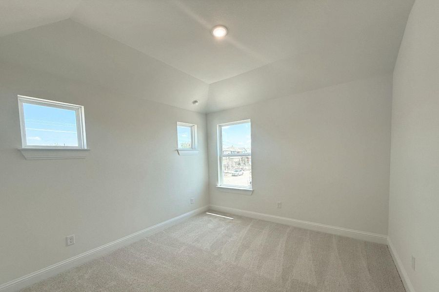 Bright room featuring neutral-toned carpet, white baseboards, and a vaulted ceiling with a recessed light Bright room featuring neutral-toned carpet, white baseboards, and a vaulted ceiling with a recessed light