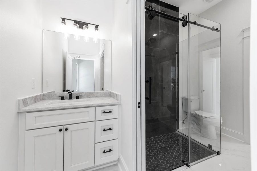 Modern bathroom featuring a sleek vanity, glass-enclosed walk-in shower, bold tile, and black finishes throughout. Modern bathroom featuring a sleek vanity, glass-enclosed walk-in shower, bold tile, and black finishes throughout.