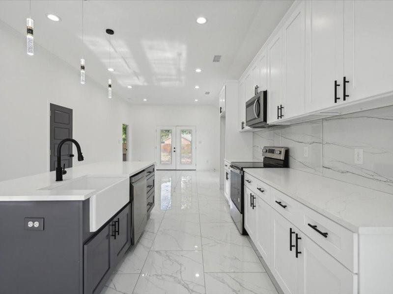 Kitchen with tasteful backsplash, light tile patterned floors, stainless steel appliances, a center island with sink, and white cabinets