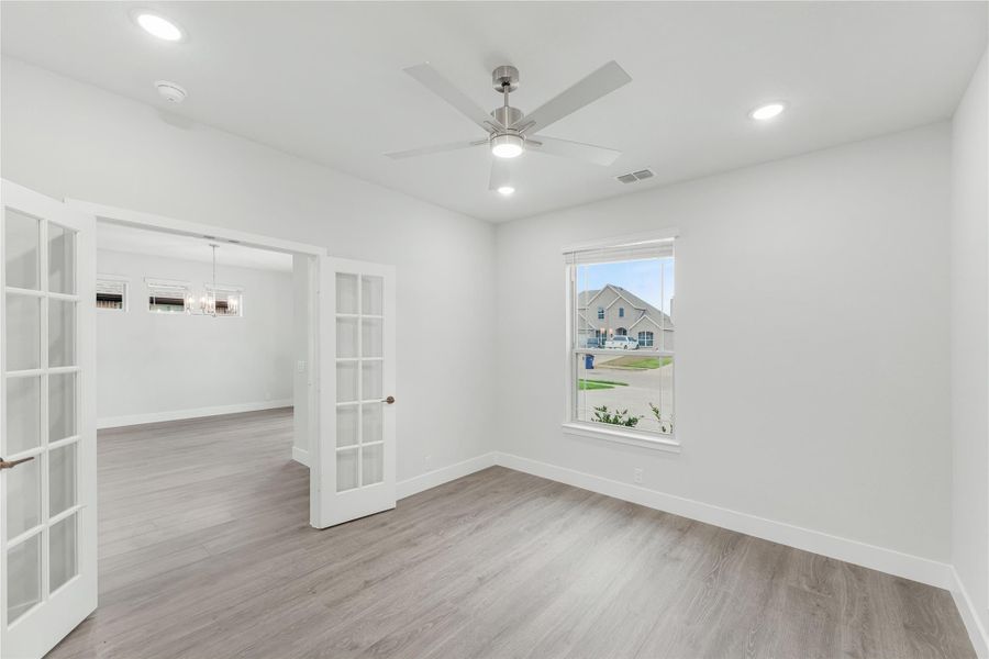 Empty room with French doors, ceiling fan, hardwood floors, and a window overlooking a neighborhood street.