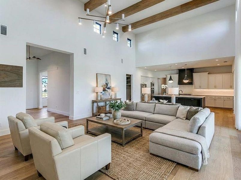 Virtual staged living room with a towering ceiling, beam ceiling, a chandelier, light wood-style floors, and a stone fireplace Virtual staged living room with a towering ceiling, beam ceiling, a chandelier, light wood-style floors, and a stone fireplace