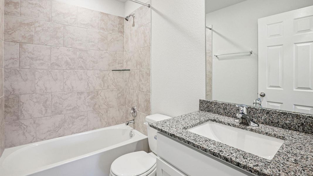 Bathroom featuring a white bathtub, beige subway tile surround, granite countertop, undermount sink, and chrome fixtures Bathroom featuring a white bathtub, beige subway tile surround, granite countertop, undermount sink, and chrome fixtures