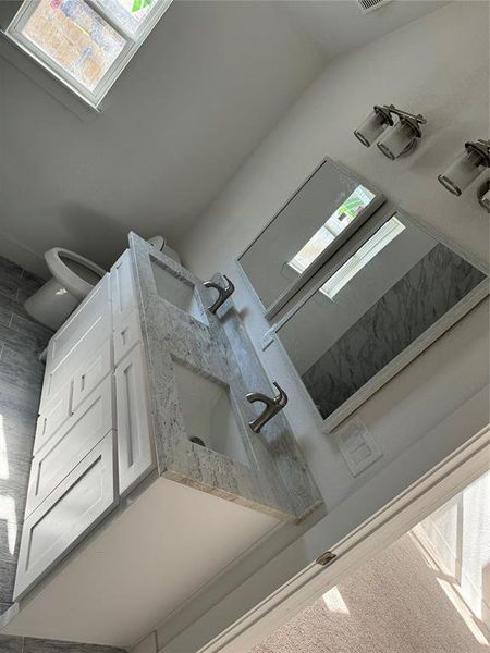 Bathroom with tile patterned flooring, lofted ceiling, toilet, and vanity