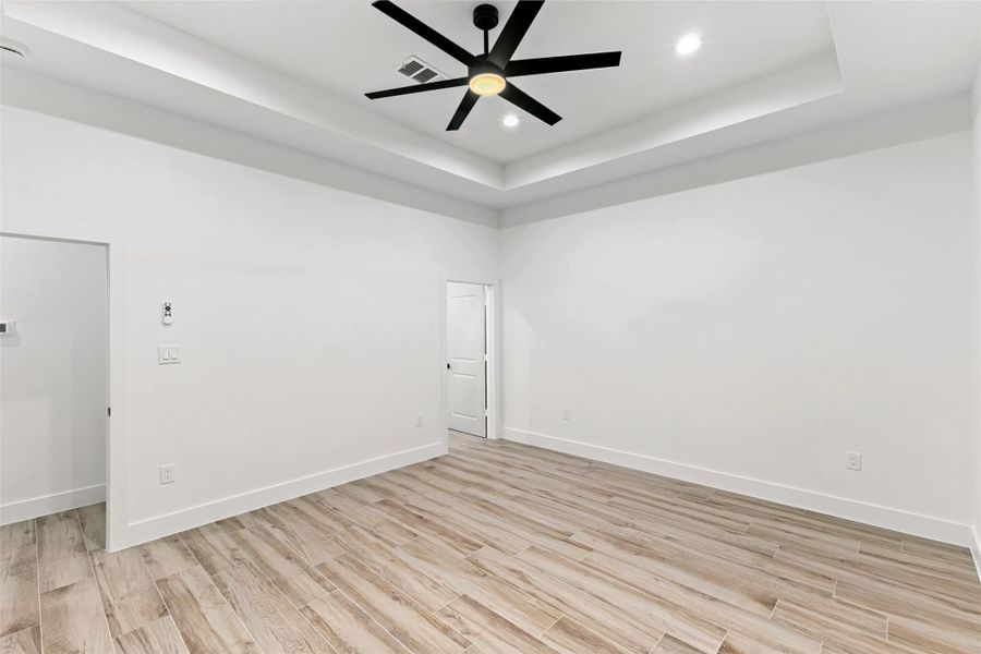 This spacious primary bedroom features light wood-look tile flooring, bright walls, and recessed lighting. It includes a modern black ceiling fan, offering a clean and contemporary feel. This spacious primary bedroom features light wood-look tile flooring, bright walls, and recessed lighting. It includes a modern black ceiling fan, offering a clean and contemporary feel.