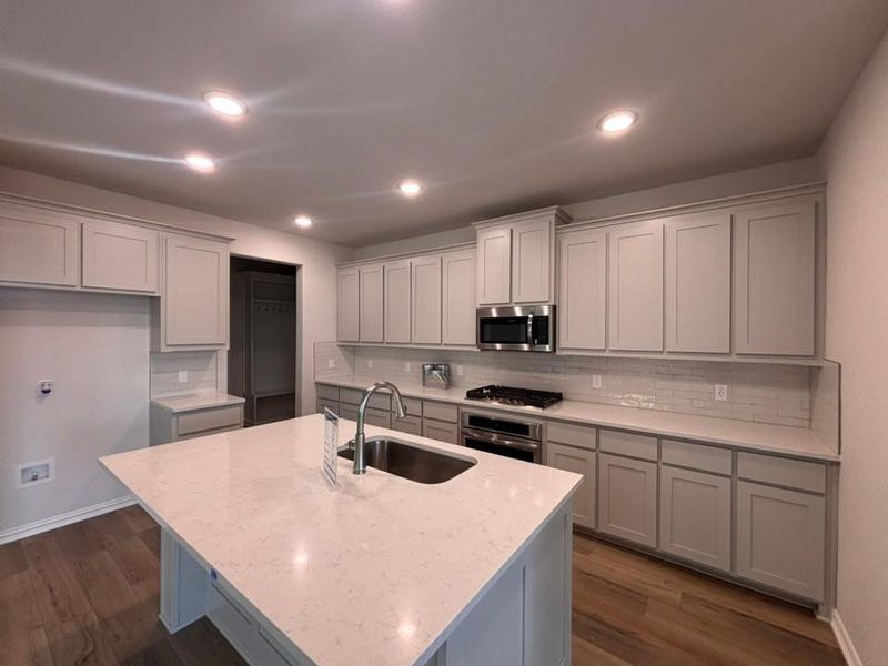 Kitchen with tasteful backsplash, dark wood-type flooring, light stone countertops, stainless steel appliances, and recessed lighting Kitchen with tasteful backsplash, dark wood-type flooring, light stone countertops, stainless steel appliances, and recessed lighting