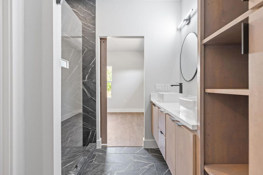 Bathroom featuring double vanity, dark marble finish floors, and a marble finish shower