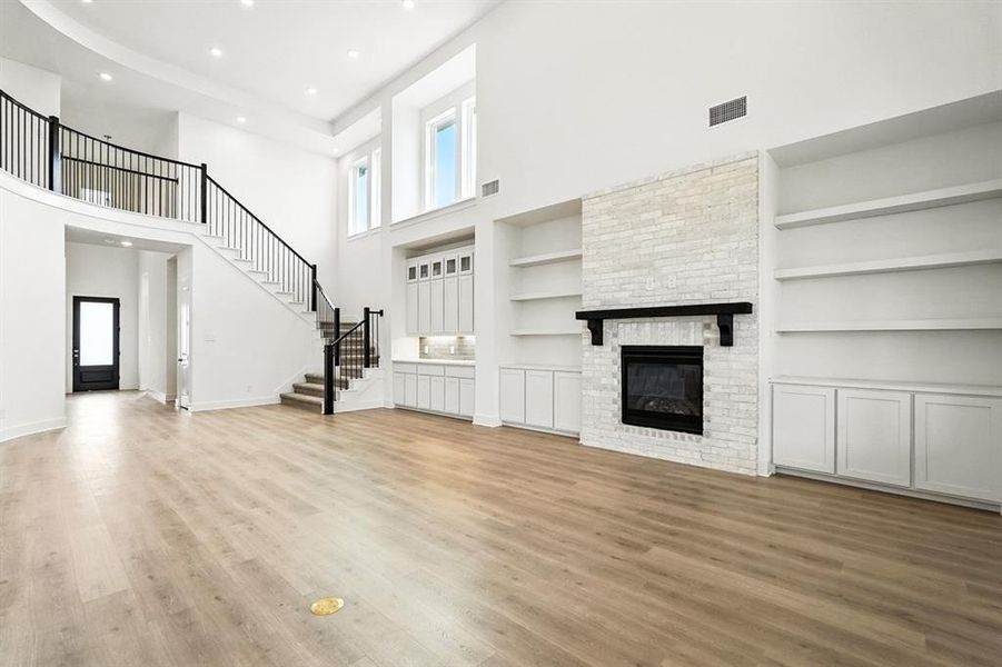 Unfurnished living room with a large fireplace, a towering ceiling, healthy amount of natural light, light wood-type flooring, and stairway Unfurnished living room with a large fireplace, a towering ceiling, healthy amount of natural light, light wood-type flooring, and stairway