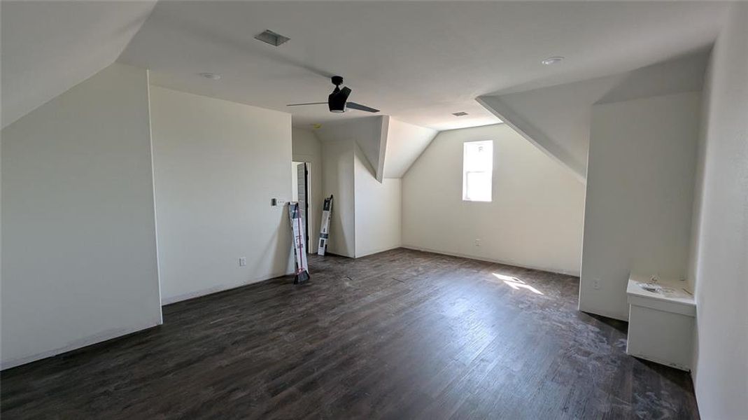 Additional living space with vaulted ceiling, dark wood-type flooring, and ceiling fan