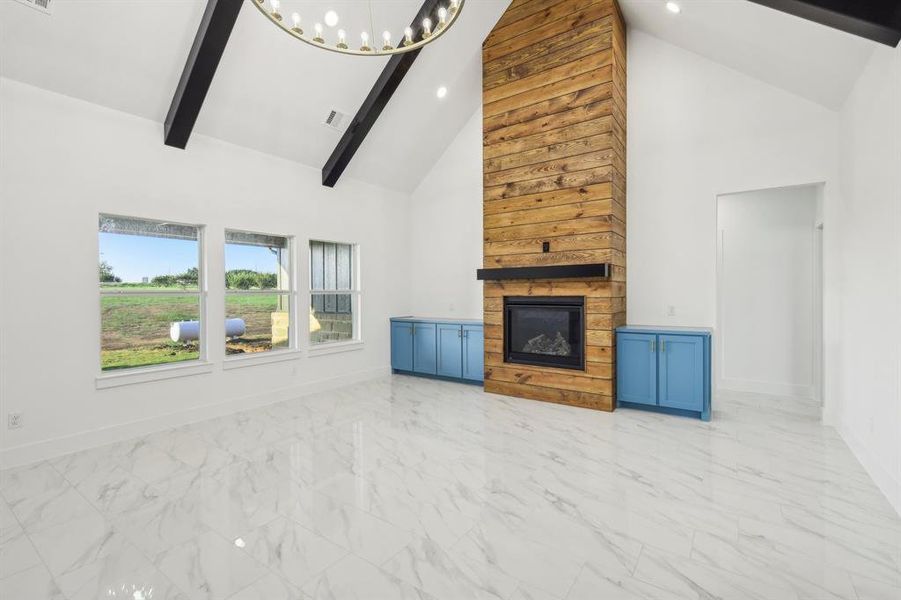 Unfurnished living room with beamed ceiling, a fireplace, high vaulted ceiling, and an inviting chandelier